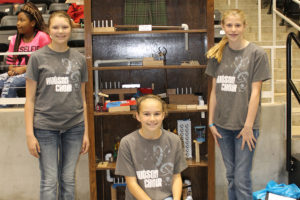 Hudson Middle School sixth-graders Nichole Flynn, Macy Puckett and Shelby King stand by their project at last Saturday’s Steamposium at Garland’s Culwell Center. The trio’s creation, which is designed to zip up the pants at the top of it, was entered in the “Rube Goldberg” portion of the contest.
